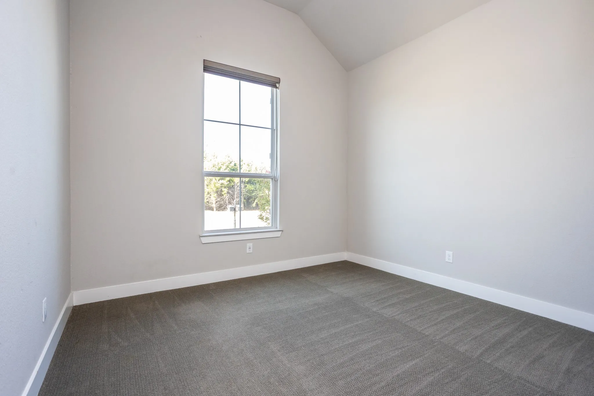 Vaulted ceiling with a large window, neutral wall paint, and gray carpet flooring