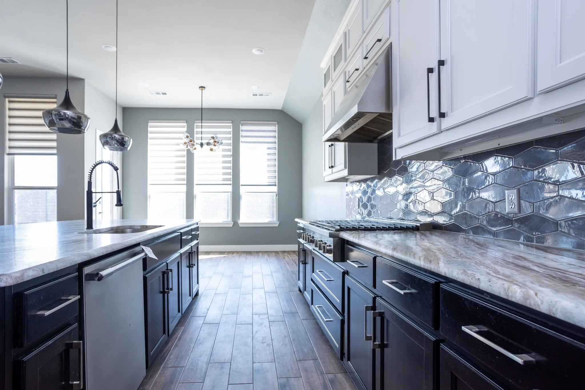 Kitchen featuring two-tone cabinetry, a textured backsplash, an island with a built-in sink, stainless steel appliances, and wood-finish flooring