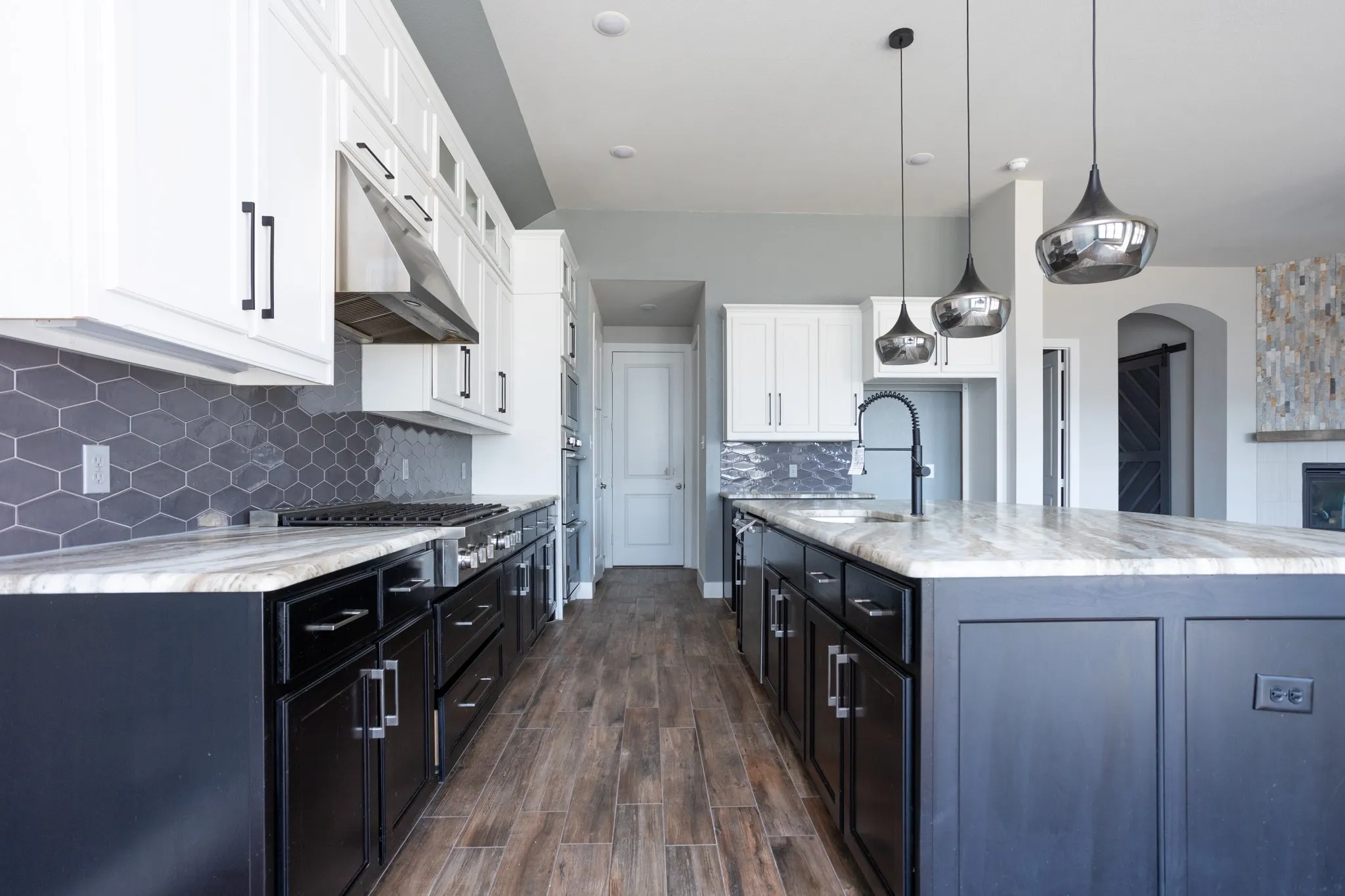 Gourmet kitchen with wood-finish flooring, two-tone cabinetry, hexagon tile backsplash, and a center island with pendant lighting