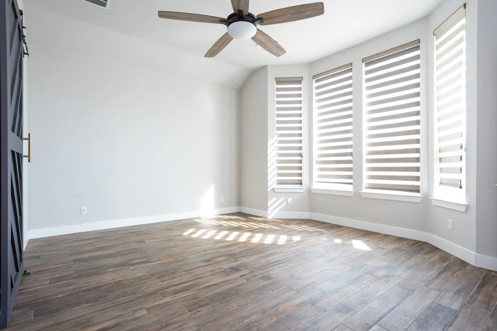 Wood-look tile flooring, bay window with multiple windows, contemporary ceiling fan, and a barn door with brass hardware
