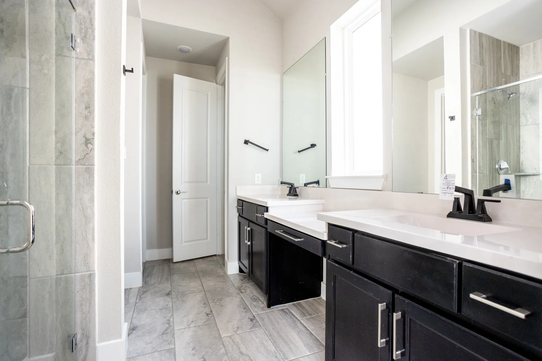 Dual vanities with white countertops and matte black fixtures, framed mirrors, and wood-finish tile flooring