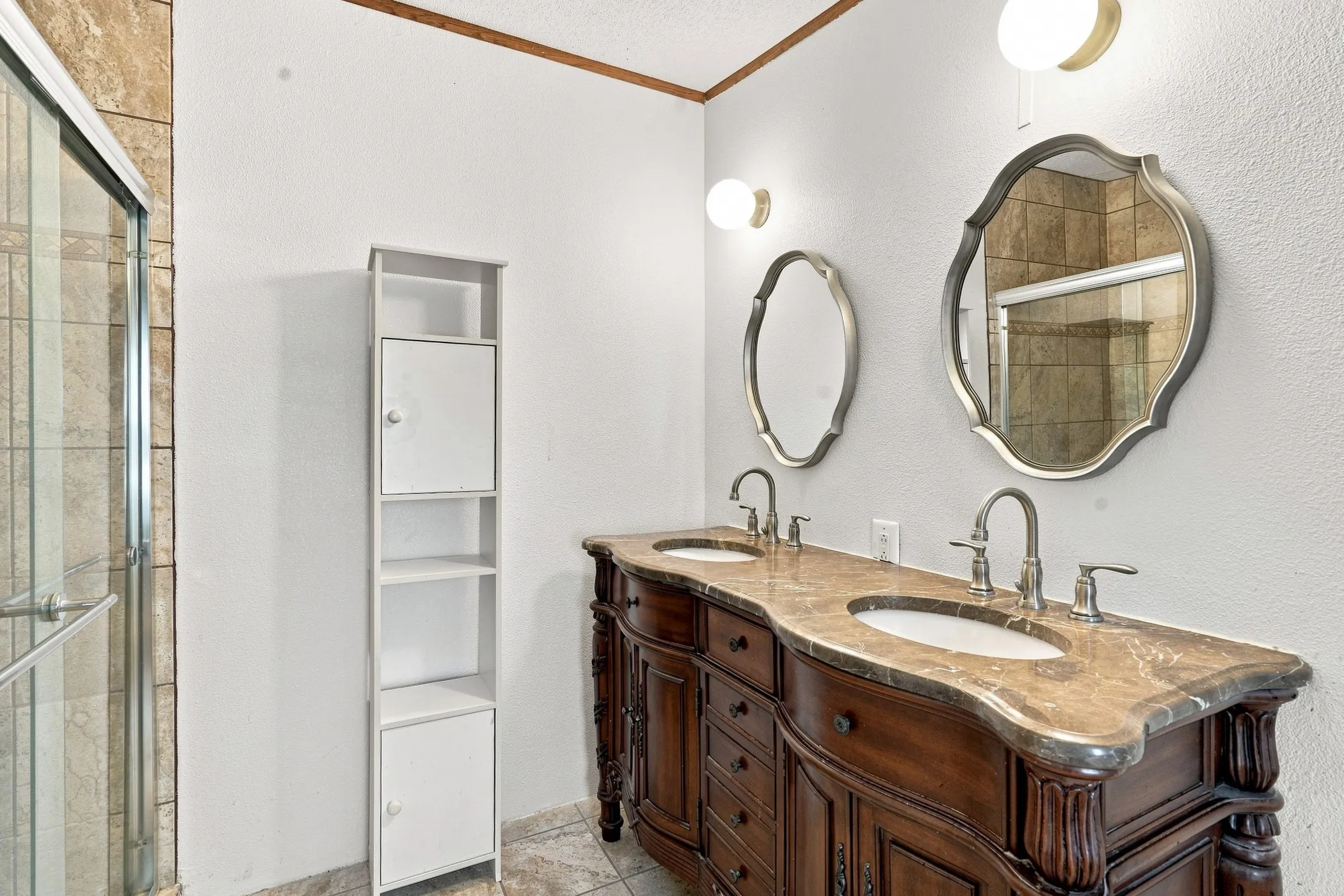 Dual vanity with carved wood-finish cabinetry, ornate framed mirrors, and a stone-finish countertop