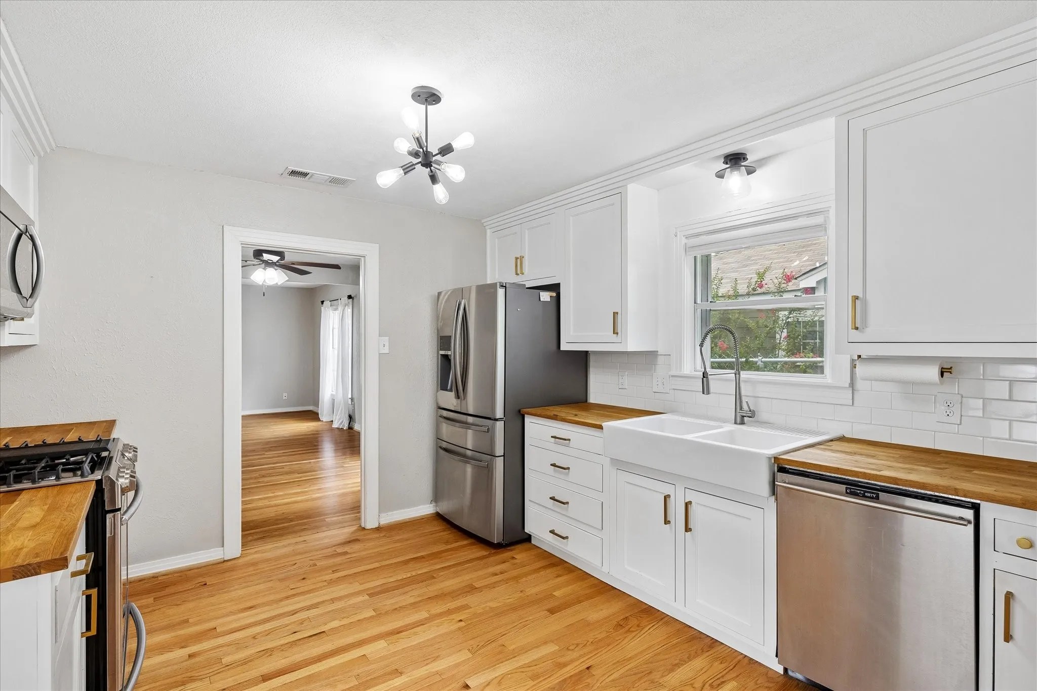 Kitchen featuring white shaker cabinetry, wood-finish countertops, stainless steel appliances, a farmhouse sink, and wood-finish flooring
