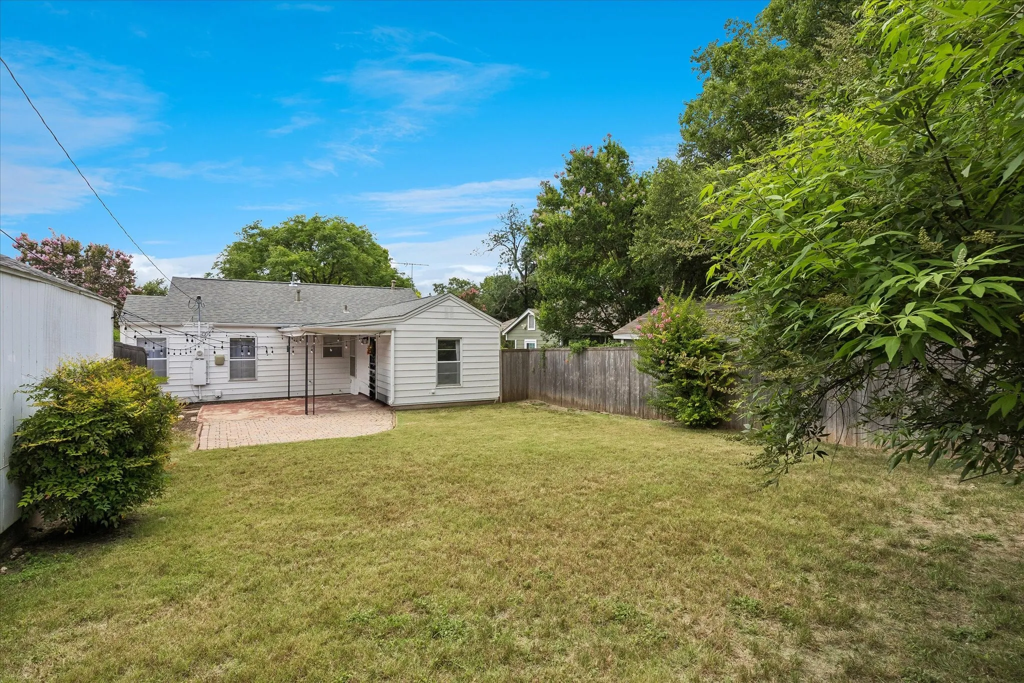 Spacious backyard with a grass lawn, privacy fencing, and a brick paver patio featuring a covered area