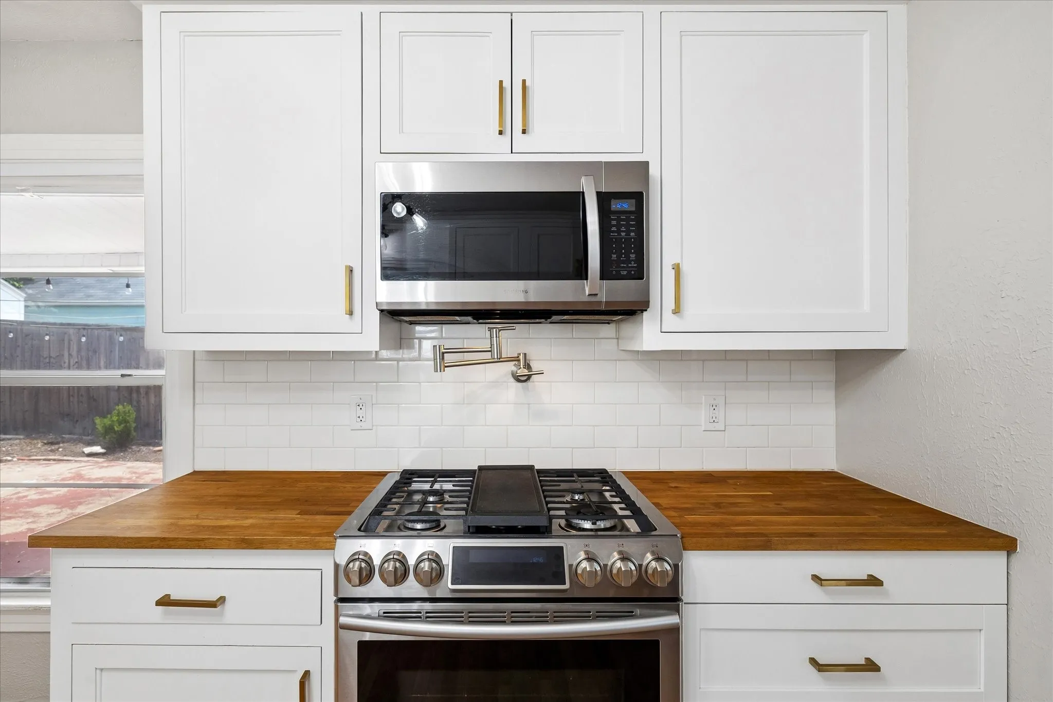 White shaker cabinetry, wood-finish countertops, stainless steel range, built-in microwave, and subway tile backsplash