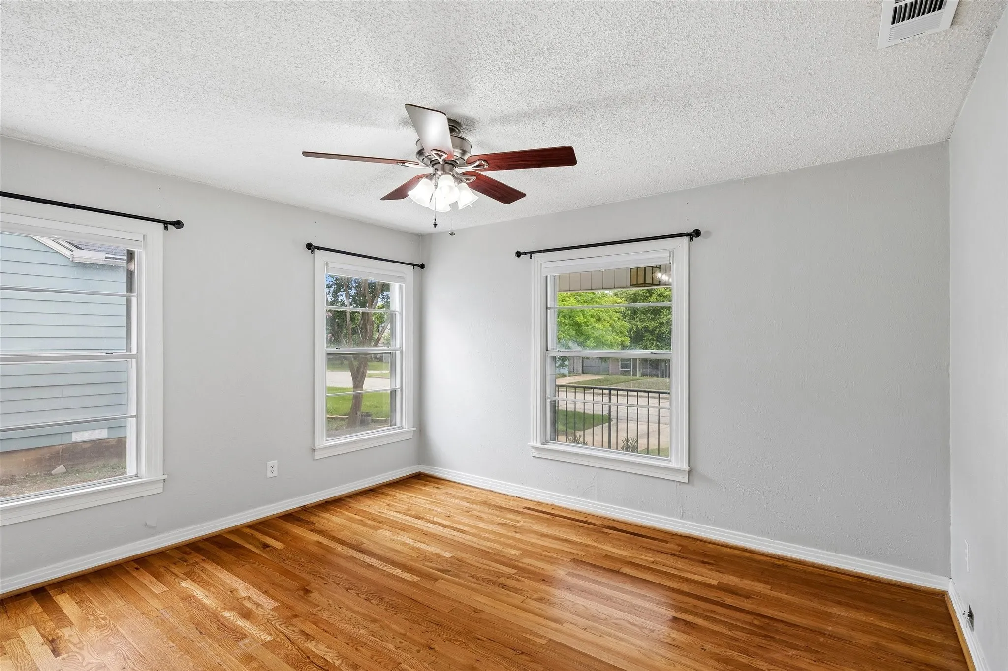 Hardwood flooring throughout, multiple windows, ceiling fan with integrated lighting, and light-colored wall finish