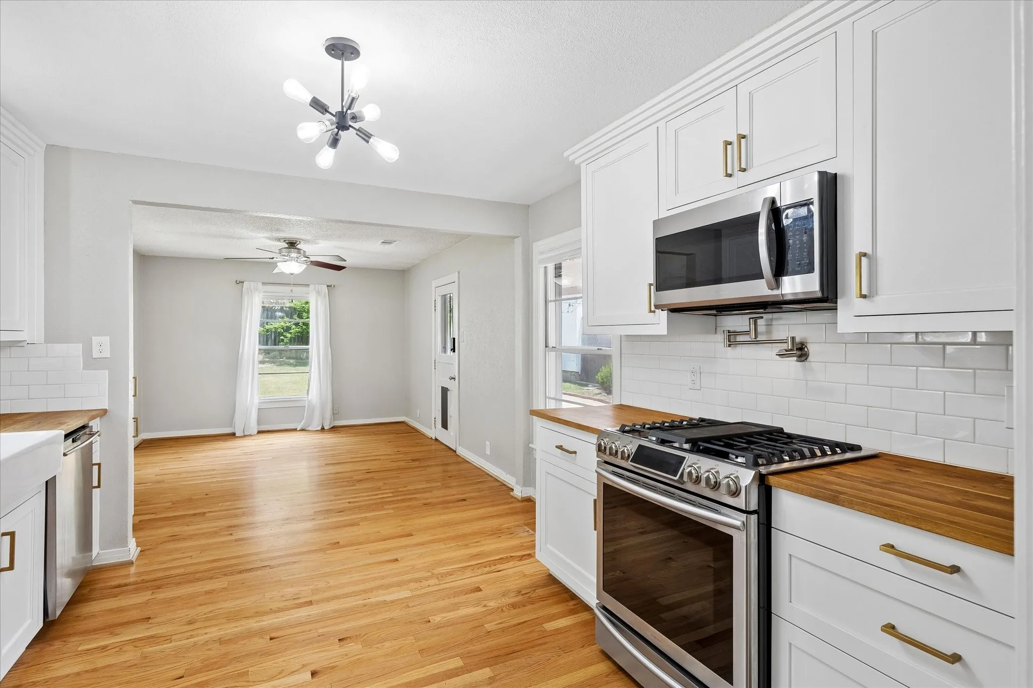 White cabinetry with gold-finish hardware, stainless steel range and microwave, wood-finish countertops, and subway tile backsplash