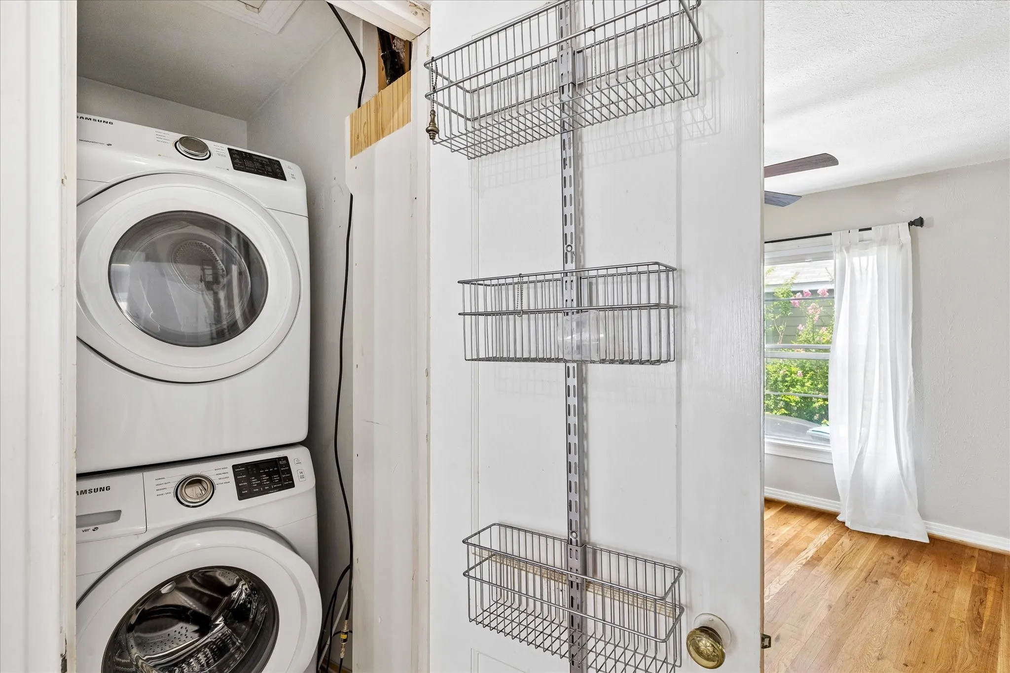 Stackable washer and dryer unit, wire shelving system, light wood-finish flooring, interior window, ceiling fan