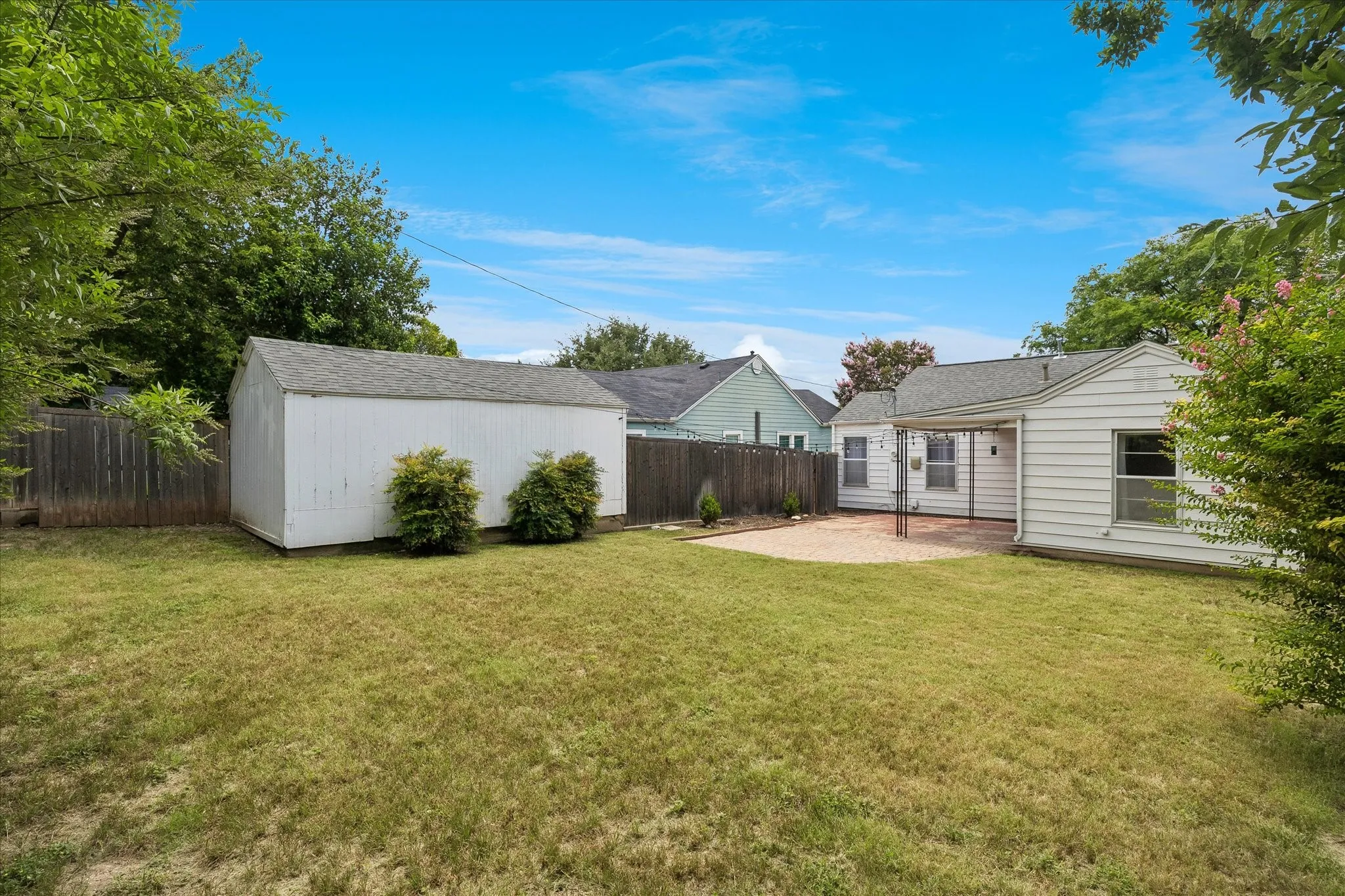 Expansive backyard featuring a manicured lawn, a detached storage shed, and a covered patio with a paved surface