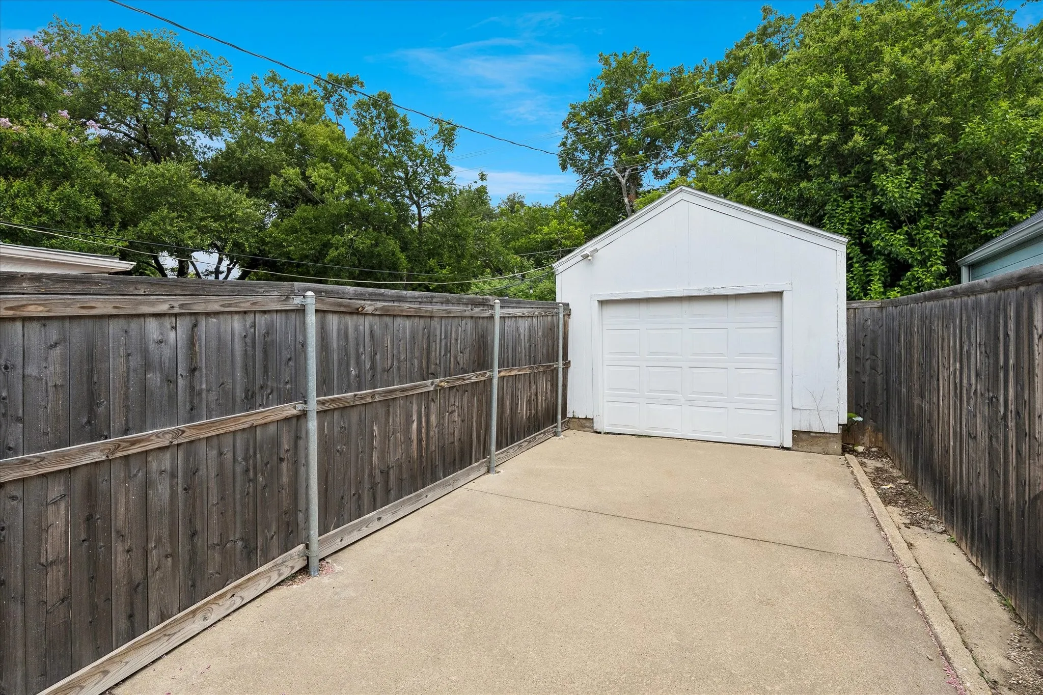 Detached garage with a paneled door, concrete driveway, and wood-panel fencing