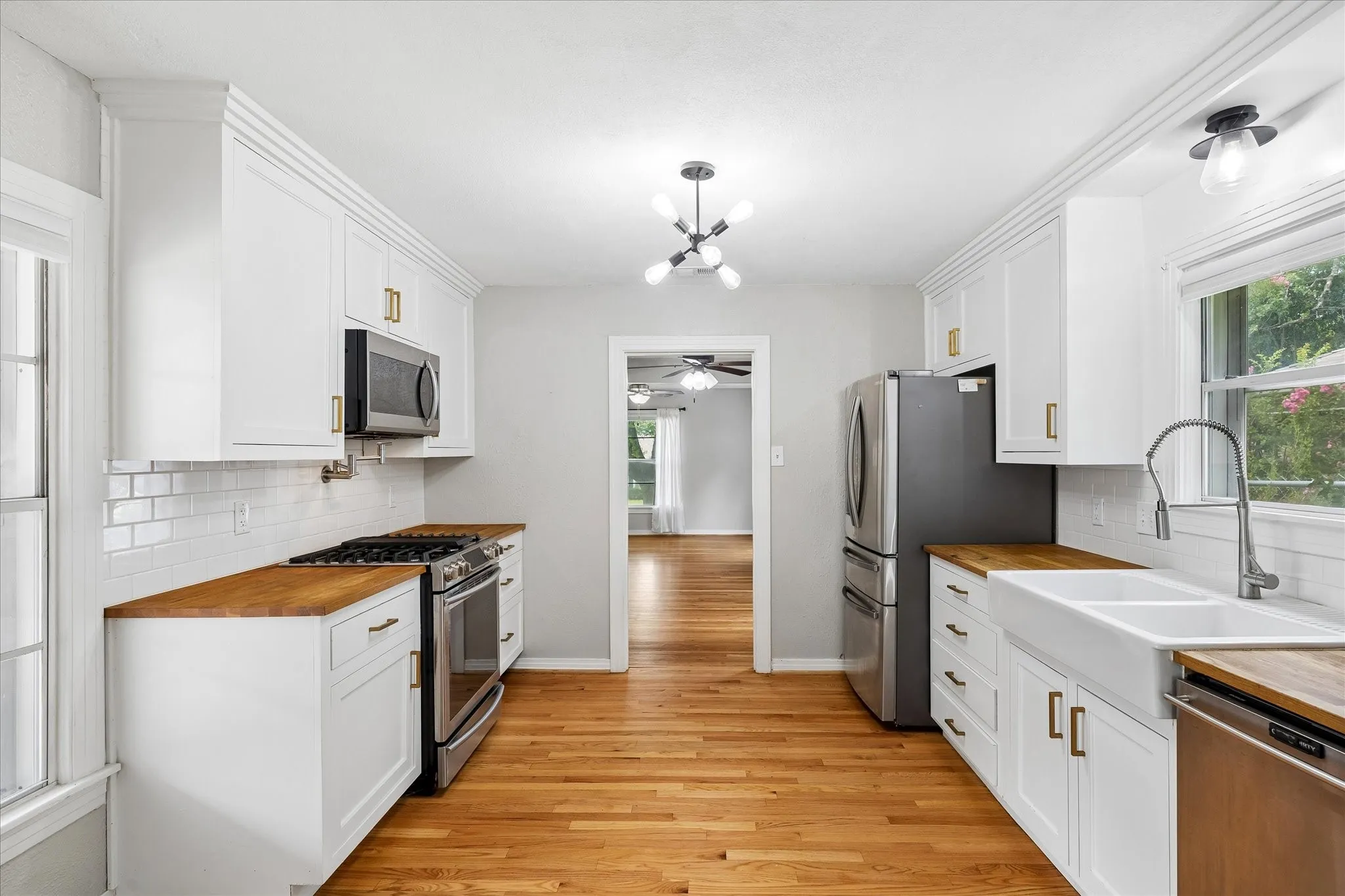 Kitchen featuring wood-finish countertops, white shaker cabinetry with gold-tone hardware, stainless steel appliances, a subway tile backsplash, and wood-finish flooring
