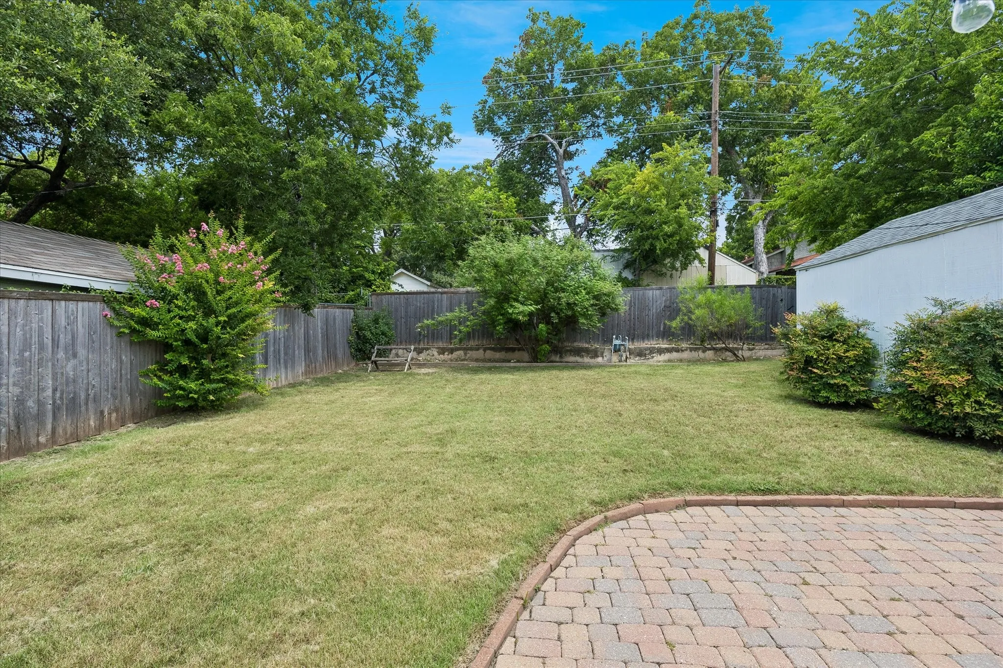Expansive green lawn with a brick paver patio, a wood privacy fence, and mature trees