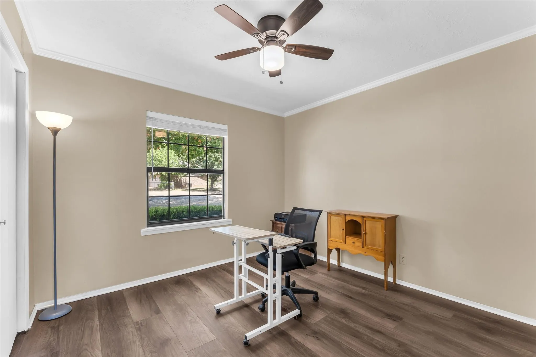 Wood-finish flooring, single window with white blinds, ceiling fan with integrated lighting, and crown molding