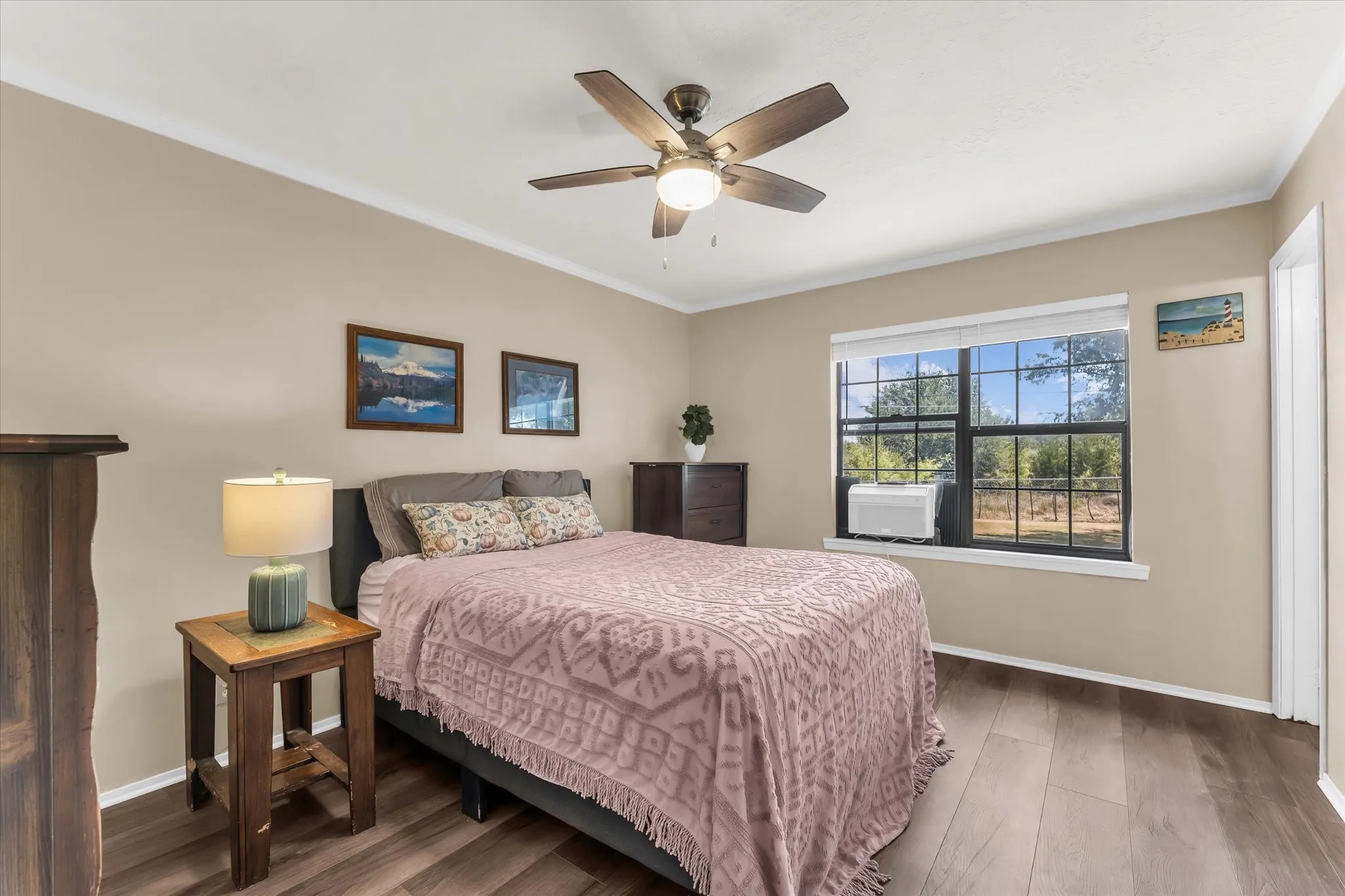 Wood-finish flooring, ceiling fan with integrated lighting, window with exterior scenery, crown molding, and neutral wall tones