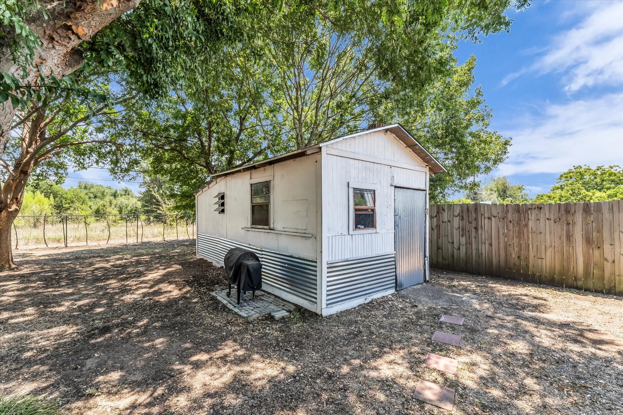Storage shed with corrugated metal siding, wood-plank fencing, and mature trees