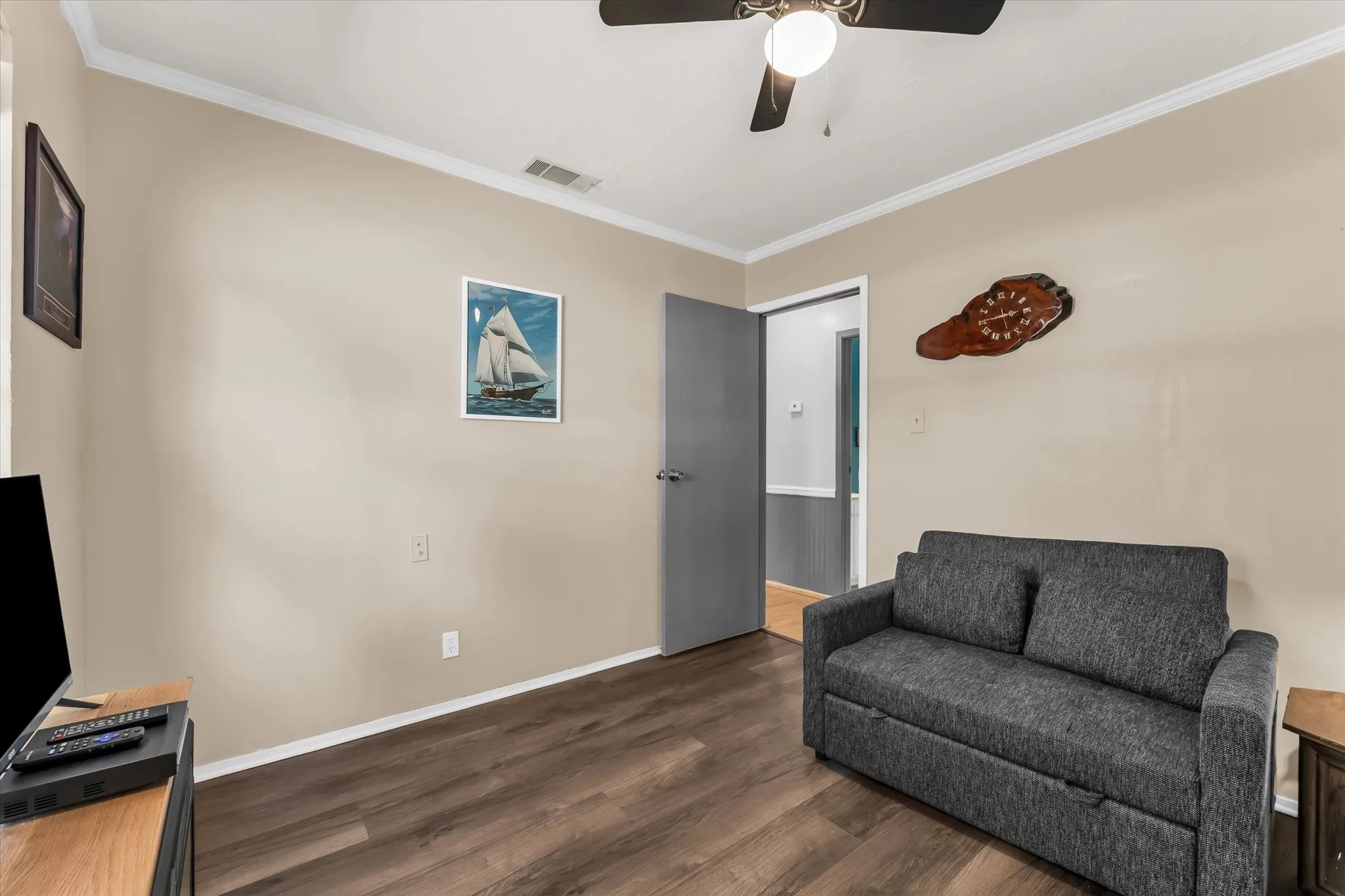Wood-finish flooring, neutral wall paint, crown molding, and a ceiling fan with integrated lighting