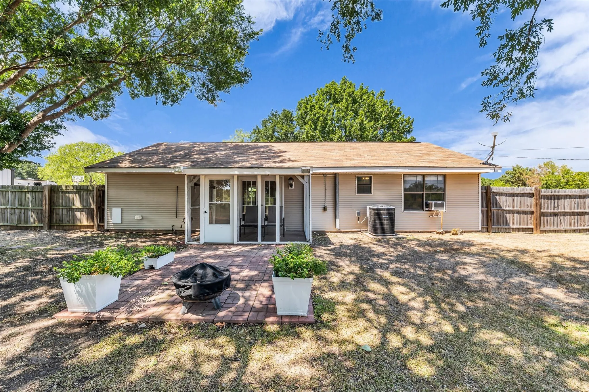 Rear exterior with a brick paver patio, screened porch entry, and wood privacy fencing