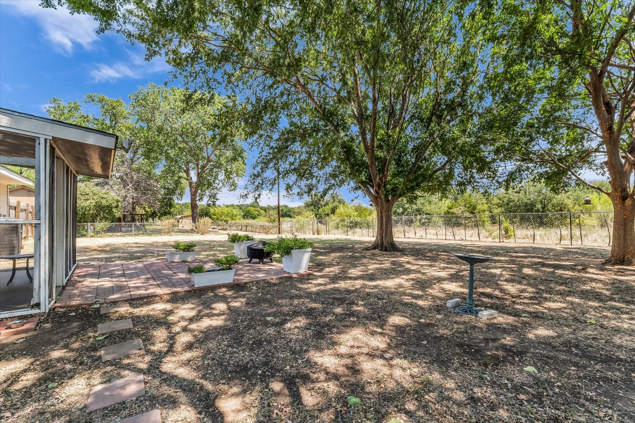Expansive outdoor area featuring a screened-in porch, brick paver patio, and mature trees providing natural shade