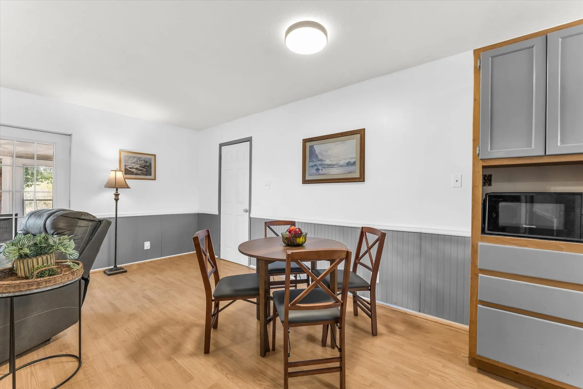 Wood-finish flooring, built-in cabinetry with gray panel doors, integrated microwave, white walls, and wainscoting