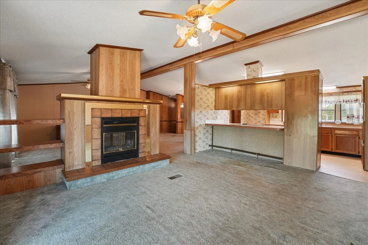 Carpeted living area featuring a fireplace with brick surround, built-in shelving, and a ceiling fan