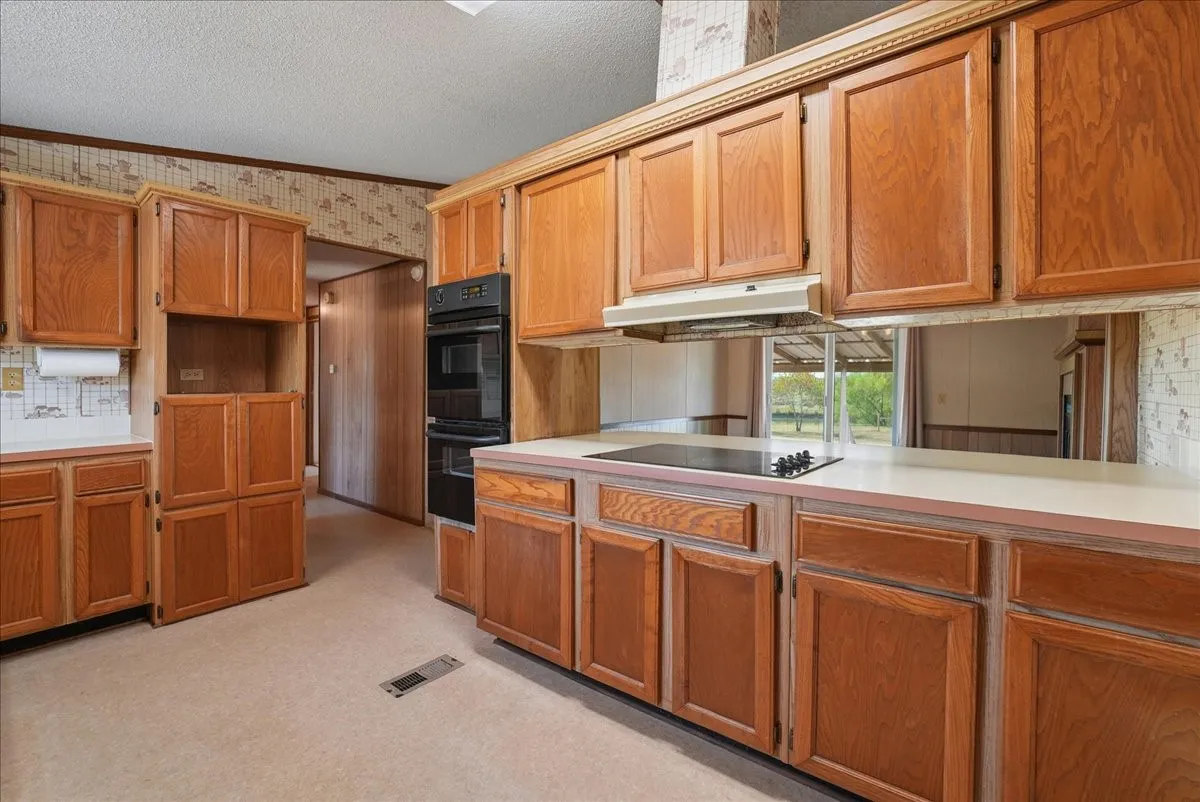 Wood cabinetry with crown molding, double wall oven, built-in cooktop, and neutral countertops