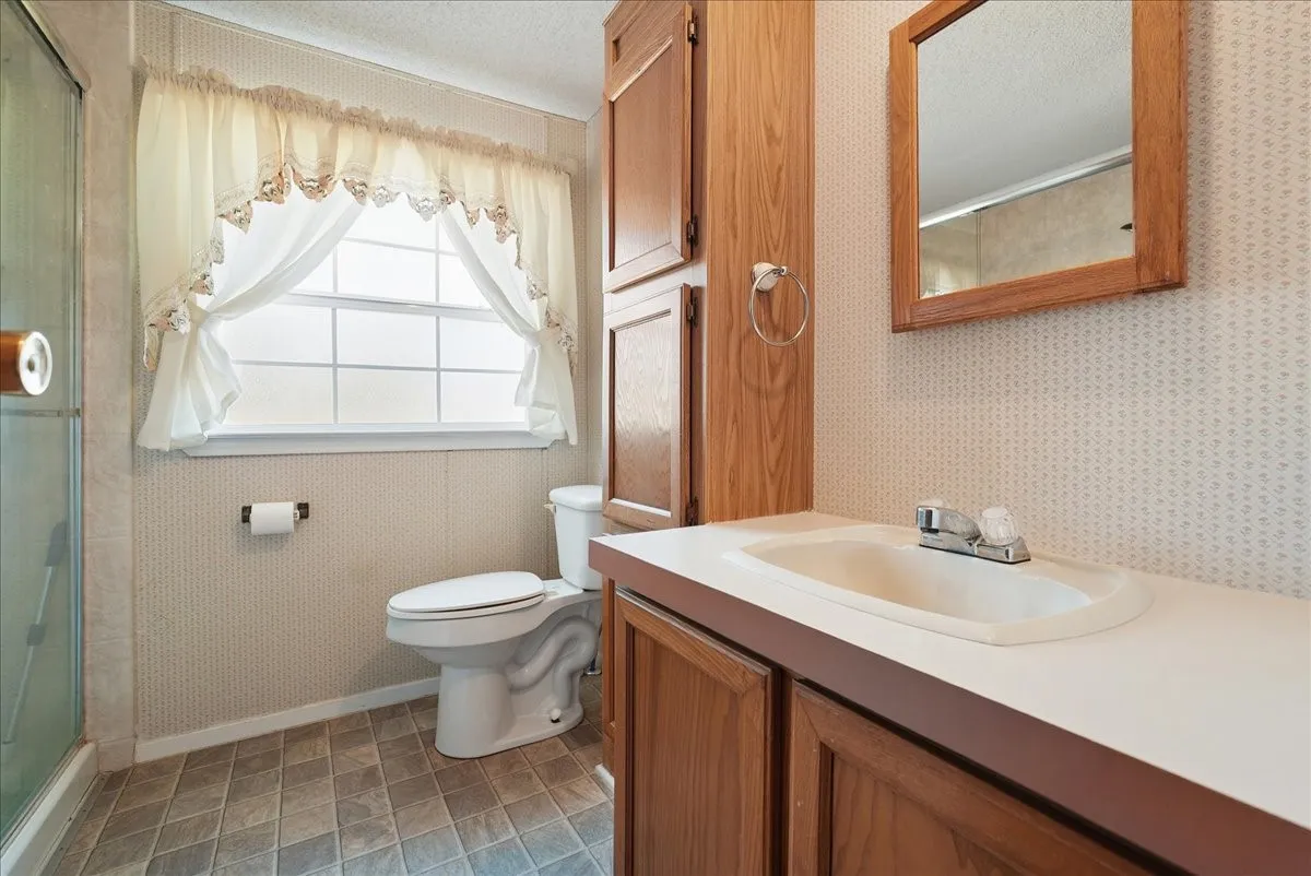 Ceramic tile flooring with a window over the toilet, a vanity with an integrated sink, and an attached wood-frame mirror