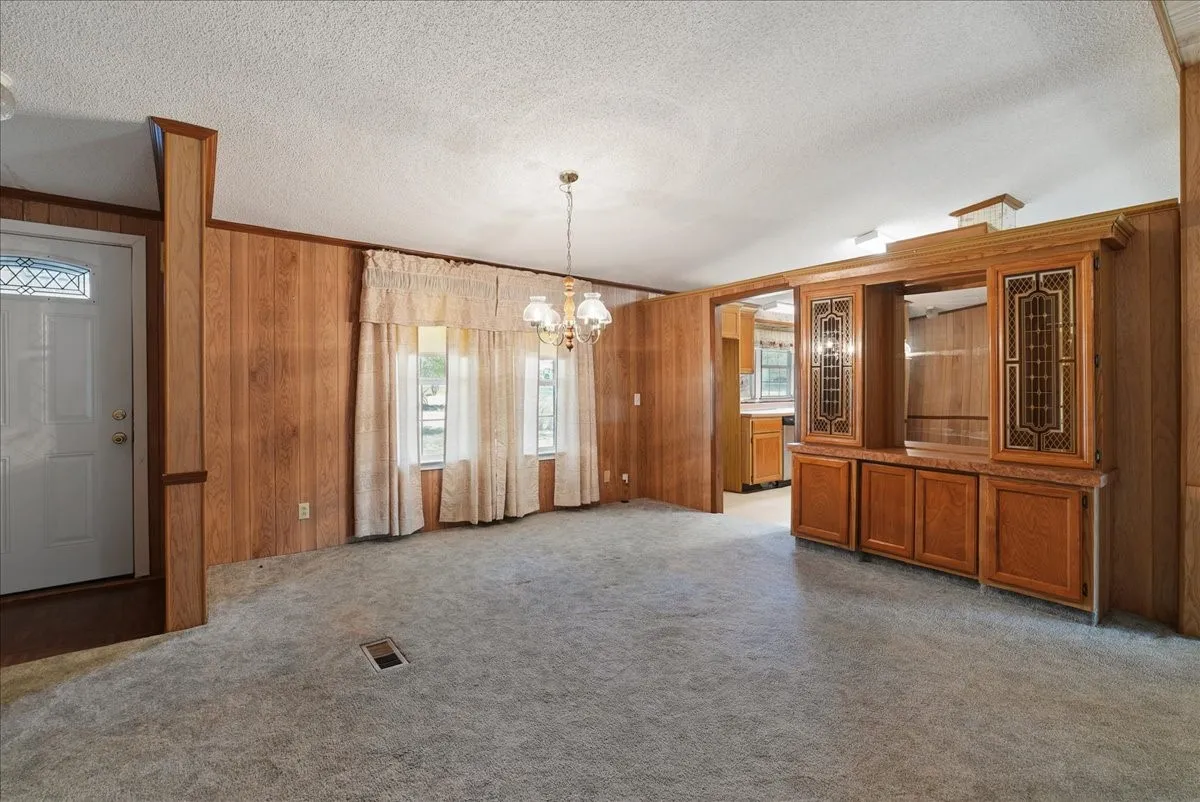 Wall paneling with wood-tone finishes, built-in cabinetry with glass inserts, white front door with decorative glass, and a chandelier lighting fixture