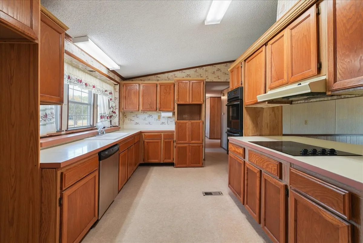 Galley kitchen featuring wood cabinetry, built-in double ovens, stainless steel dishwasher, and a countertop cooktop