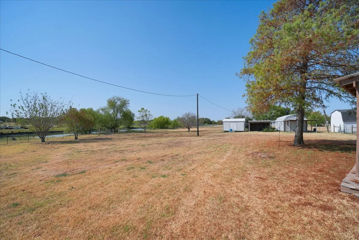 Expansive yard featuring a large tree, multiple outbuildings, and a perimeter fence