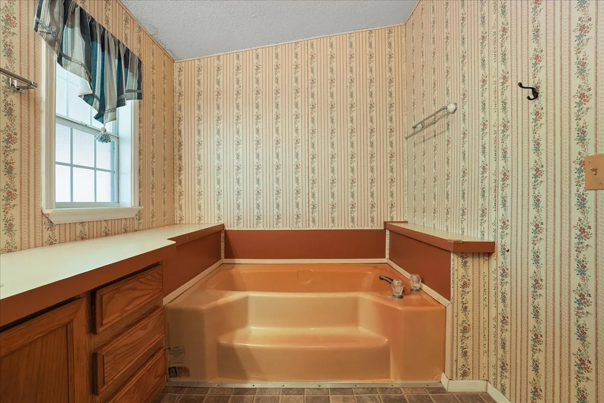 Built-in soaking tub with steps, integrated countertop, and wood-finish cabinetry
