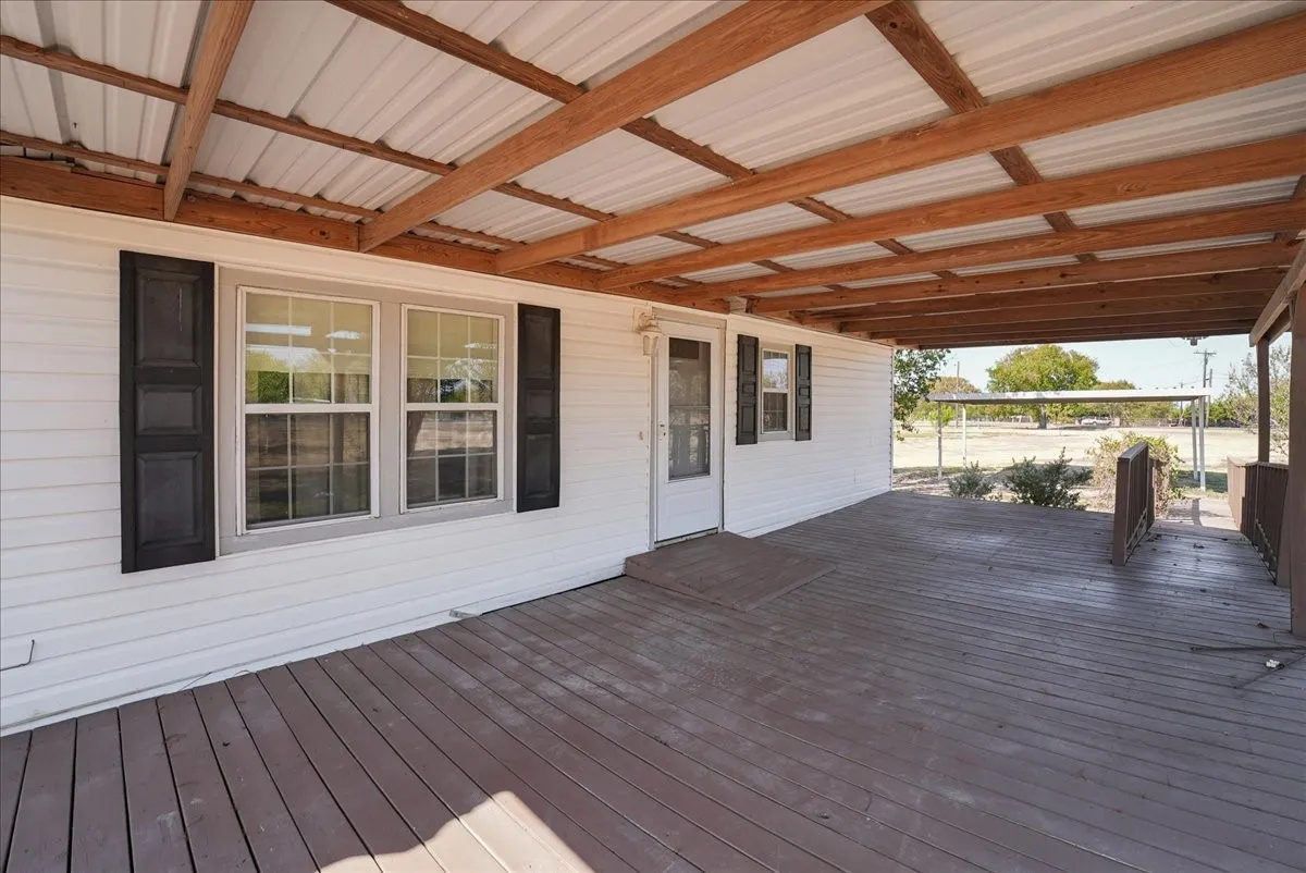 Expansive covered porch featuring wood decking, exposed wood beams, and a corrugated metal roof
