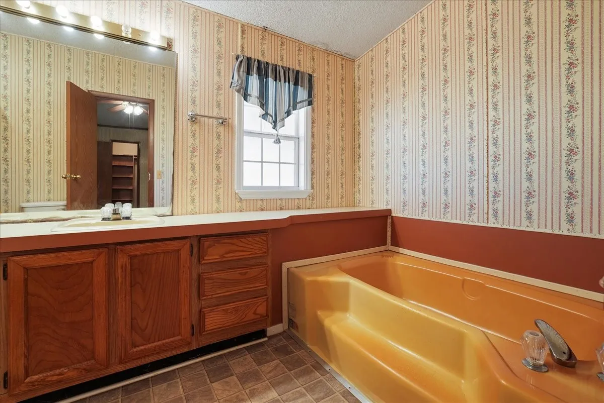 Bathroom featuring a built-in bathtub, a window, a vanity with wood-finish cabinetry, and a large wall-mounted mirror