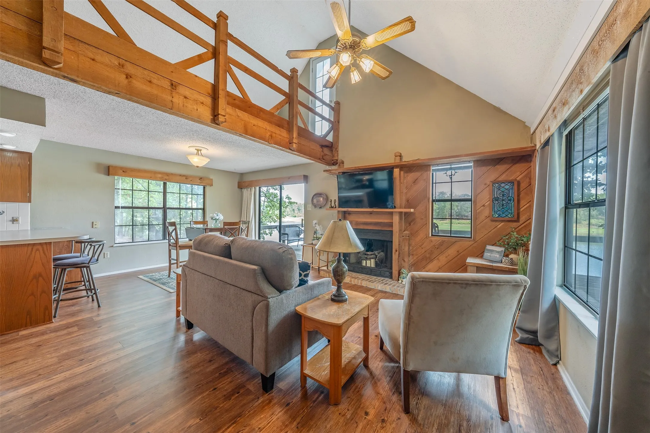 Vaulted ceiling with exposed wood beams, wood-finish flooring, fireplace, wood paneling, and a built-in ceiling fan