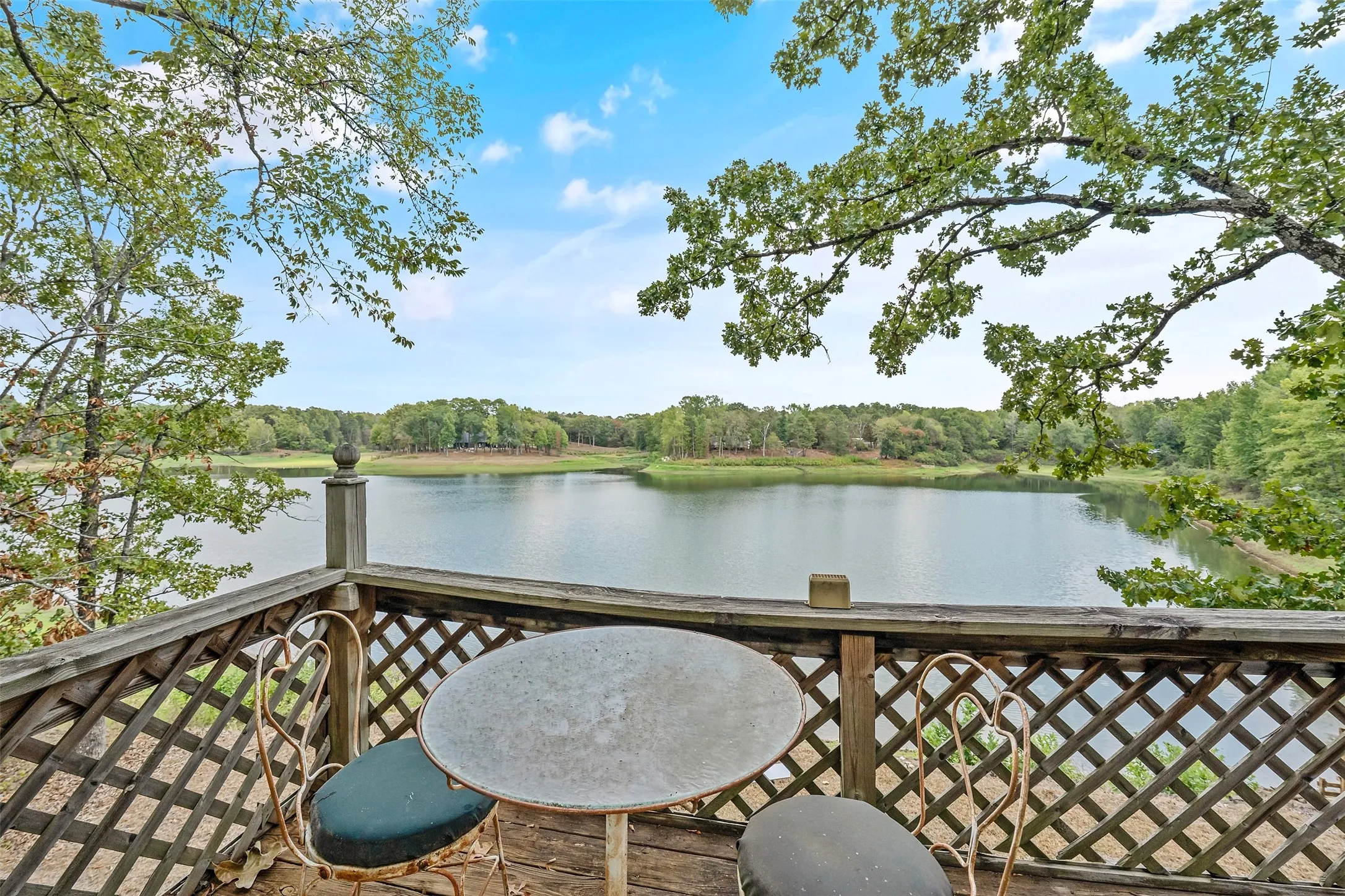 Expansive water feature, surrounding mature trees, and a wooden deck with lattice railing