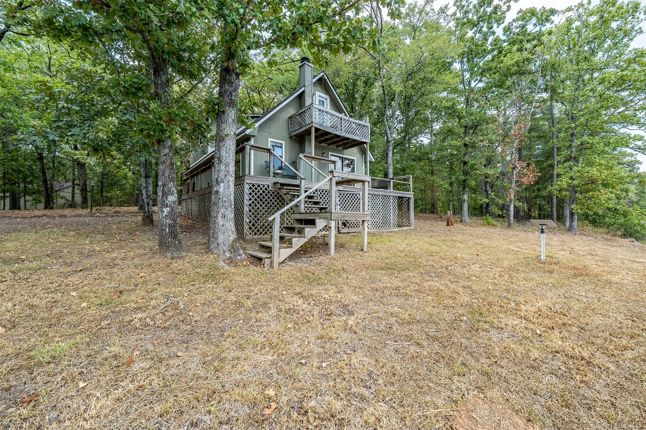 Two-story residence with a light green exterior, multiple wooden decks, and surrounding mature trees