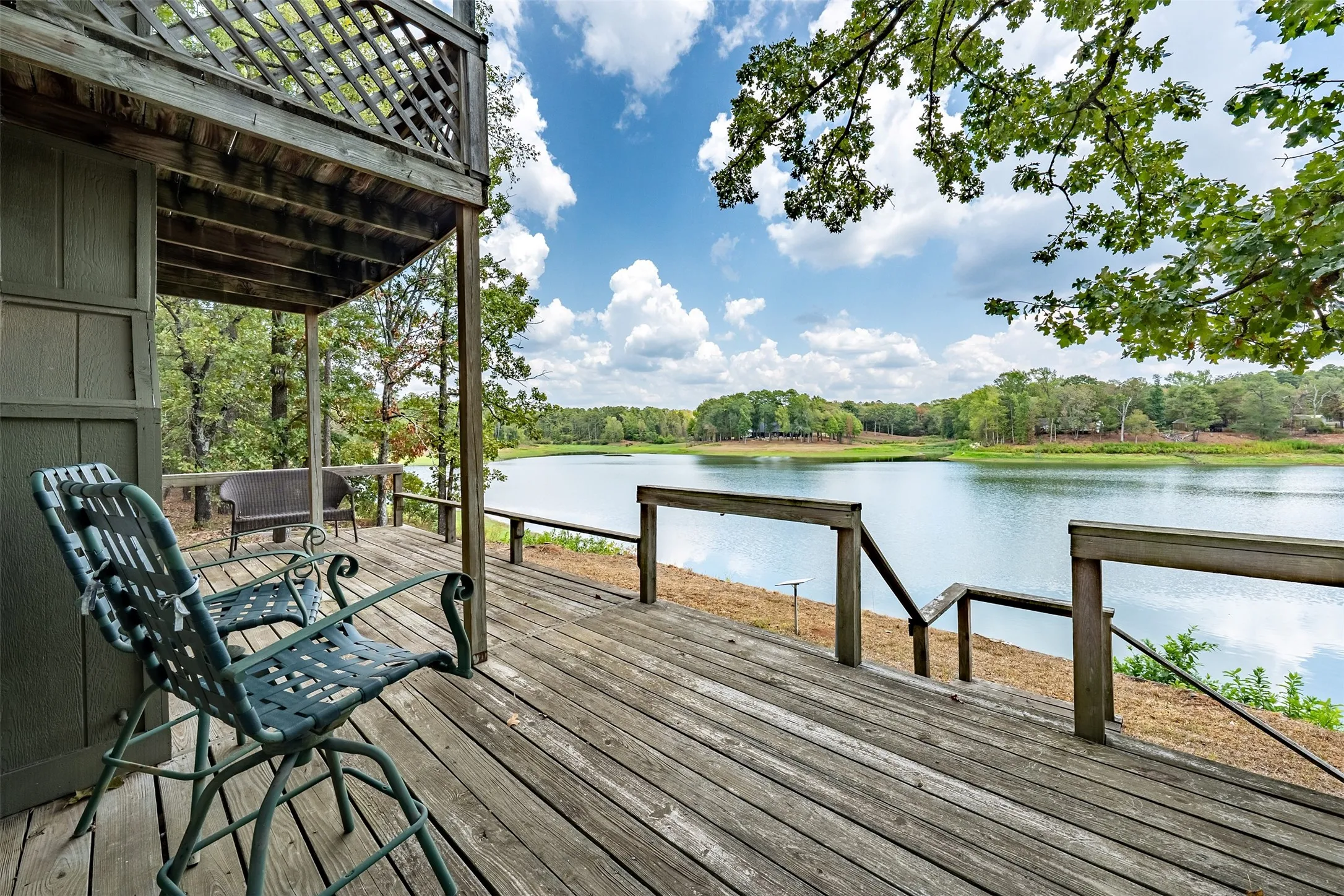 Expansive wood-finish deck with direct water frontage, featuring a lake and surrounding trees