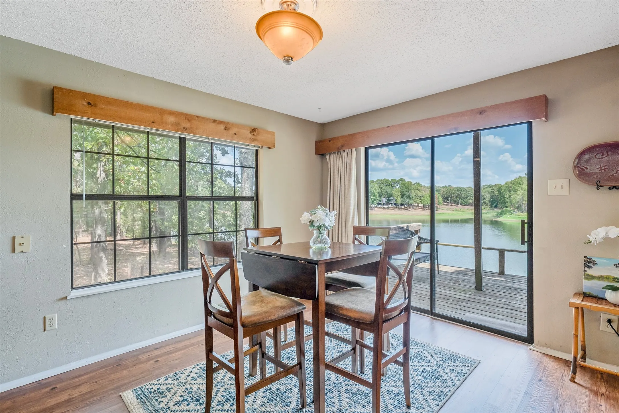 Sliding glass door leading to a waterfront deck, large picture window, wood-finish flooring, and recessed ceiling light fixture
