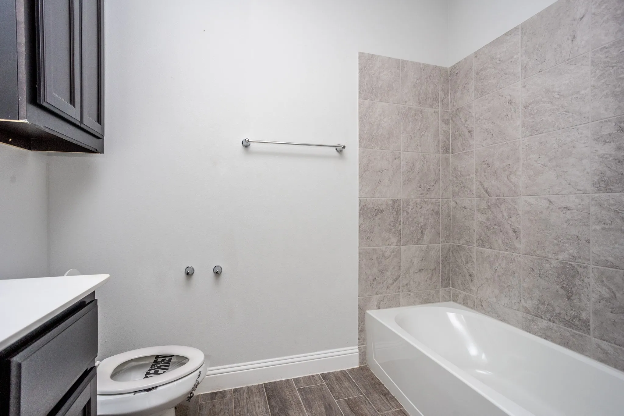 White bathtub with tiled surround, wood-finish flooring, and white baseboards