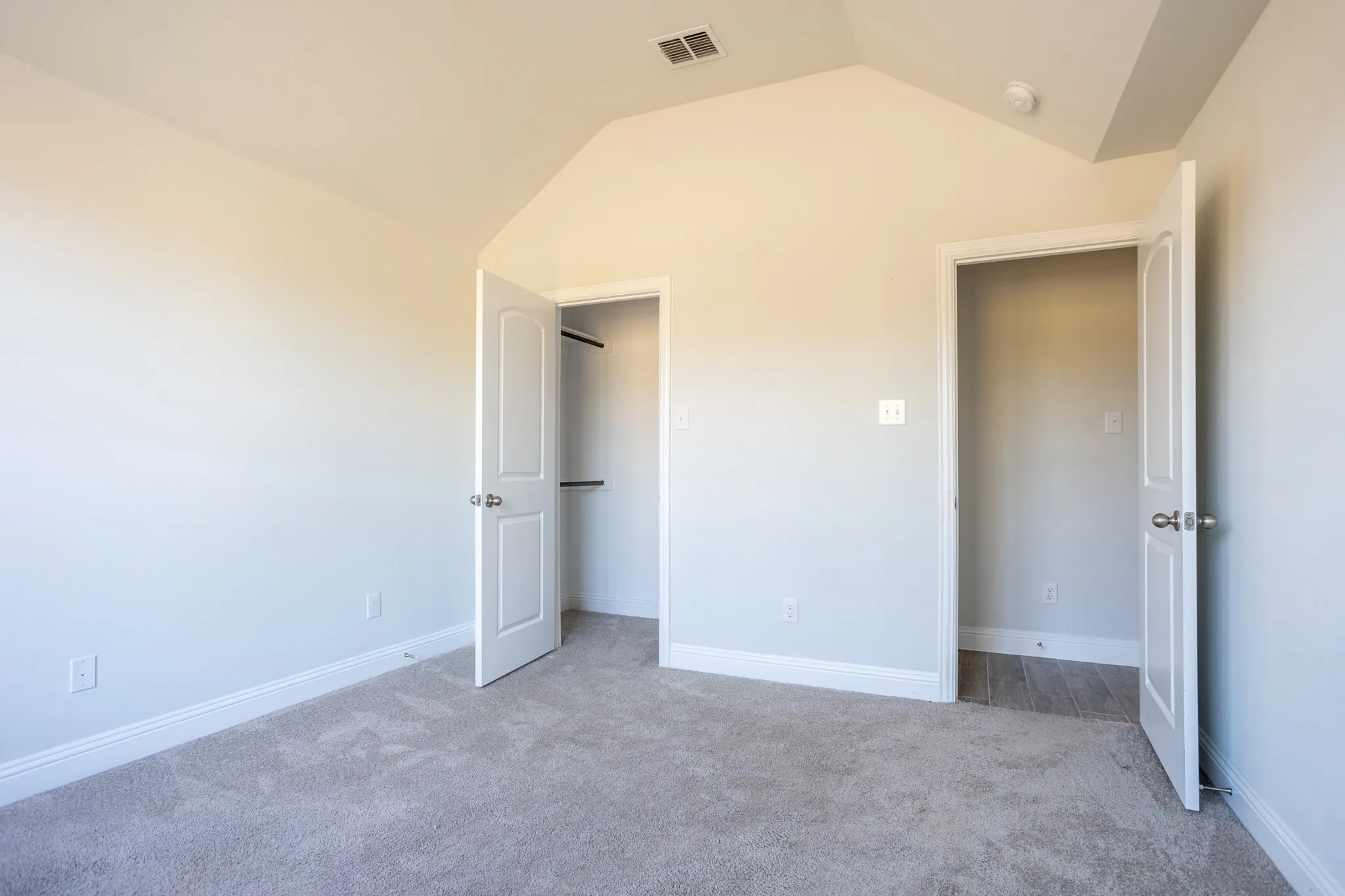 Vaulted ceiling, two paneled doors, two closets with hanging rods and shelving, and neutral carpeting