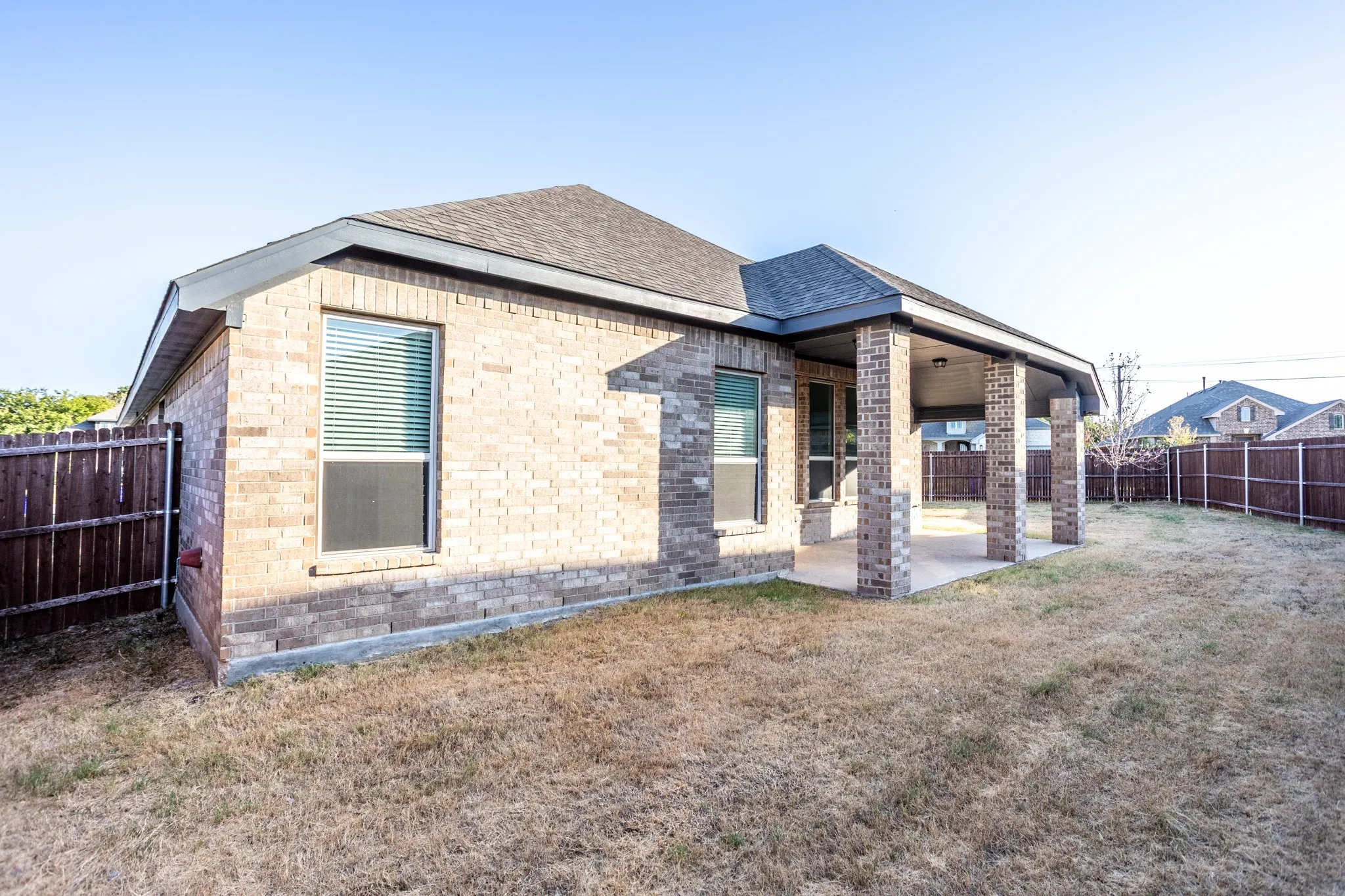 Brick exterior featuring a covered patio with supporting columns, a privacy fence, and a shingle roof