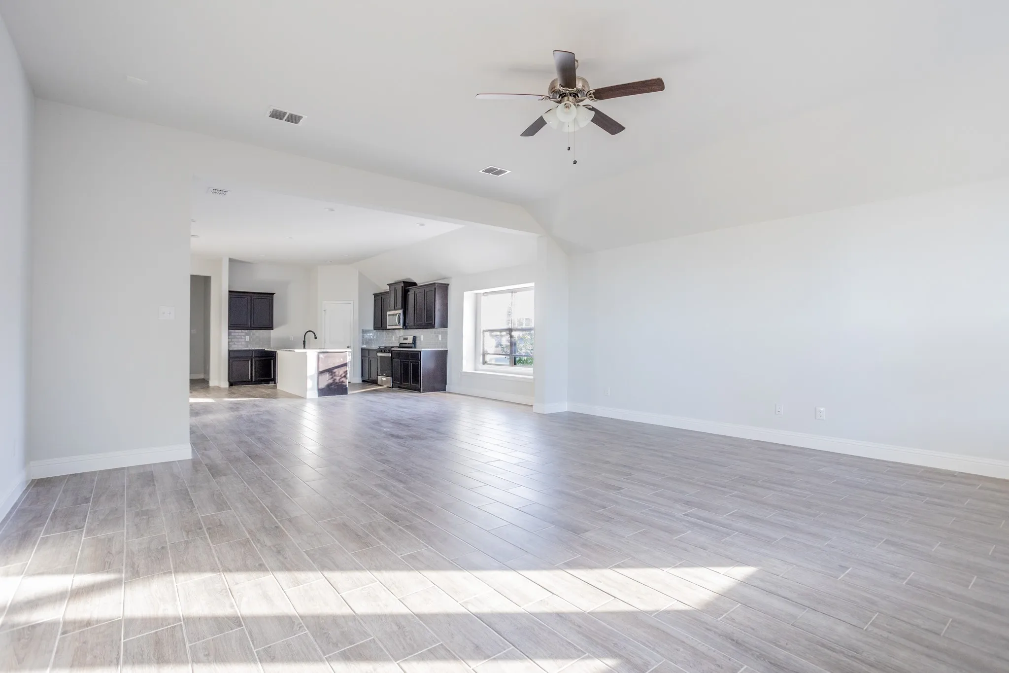 Expansive room featuring wood-finish tile flooring, vaulted ceilings, and a ceiling fan