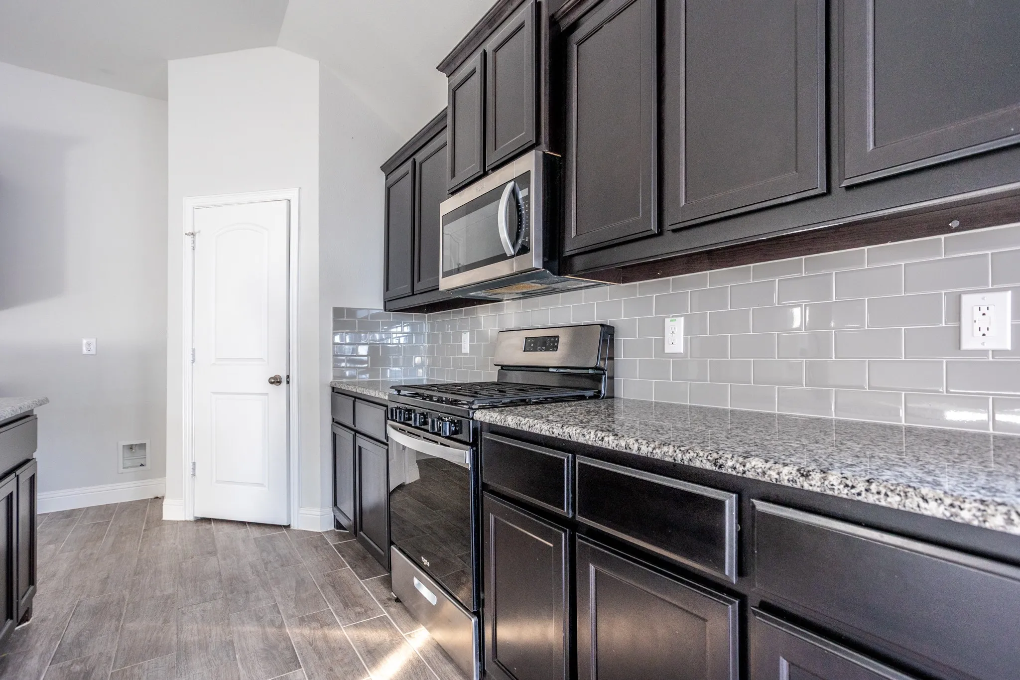 Kitchen featuring dark cabinetry, stainless steel appliances, speckled countertops, and a subway tile backsplash