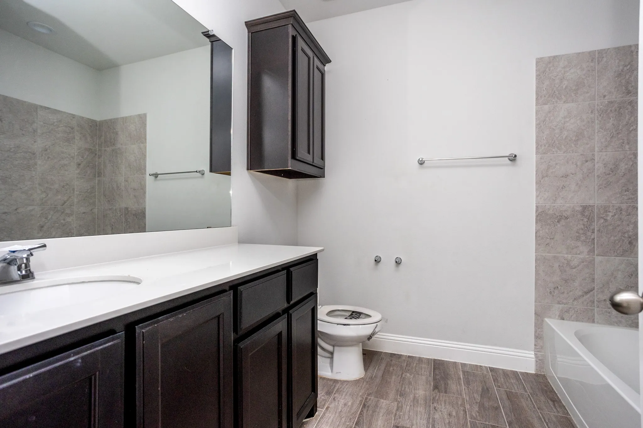 Wood-finish flooring, dark wood cabinetry, white countertop, integrated sink, and tiled shower​​‌​​​​‌​​‌‌​‌‌​​​‌‌​‌​‌​‌​​​‌​​ surround