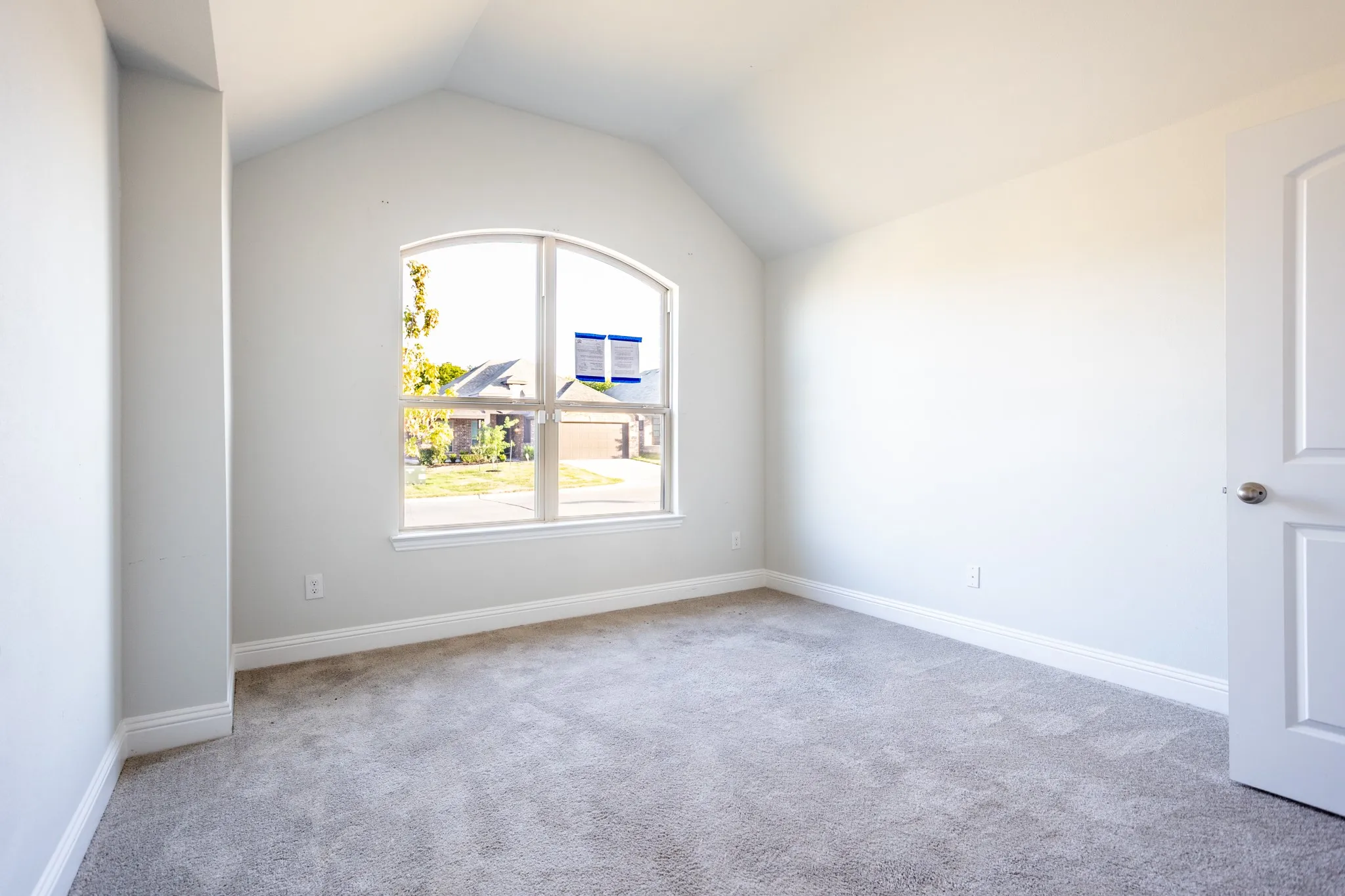 Arched window, vaulted ceiling, neutral gray carpet, white trim, and a white paneled door