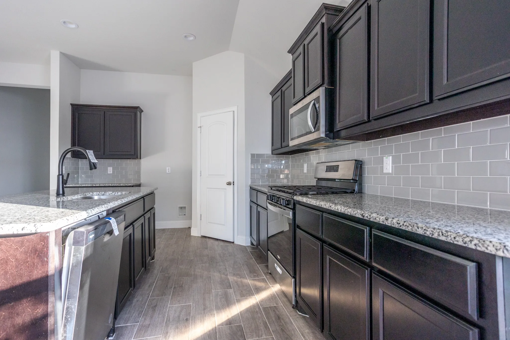 Kitchen featuring dark cabinetry, speckled countertops, stainless steel appliances, a subway tile backsplash, and wood-finish flooring