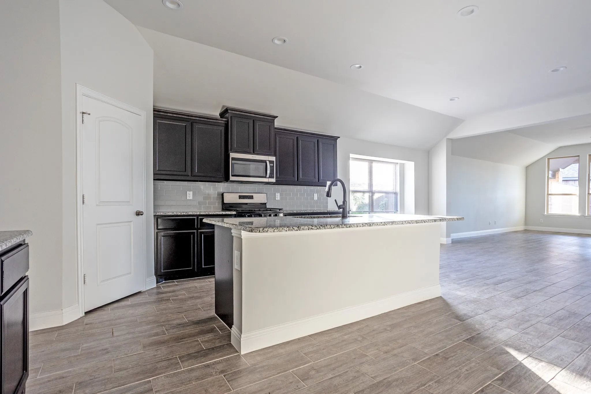 Kitchen with dark cabinetry, stainless steel appliances, granite countertops, and a subway tile backsplash