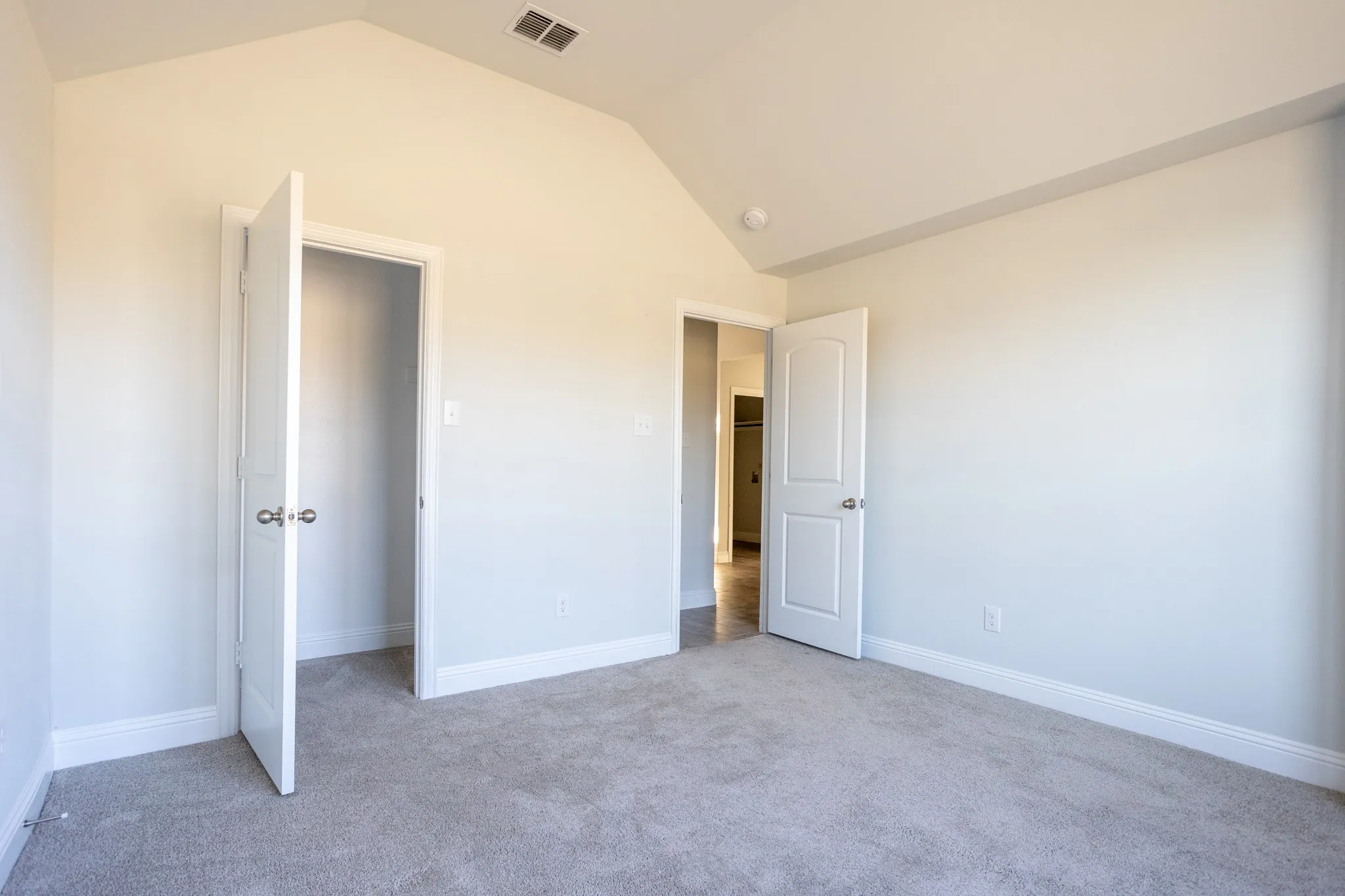 Vaulted ceiling, neutral wall paint, gray carpet flooring, white trim, and white paneled doors