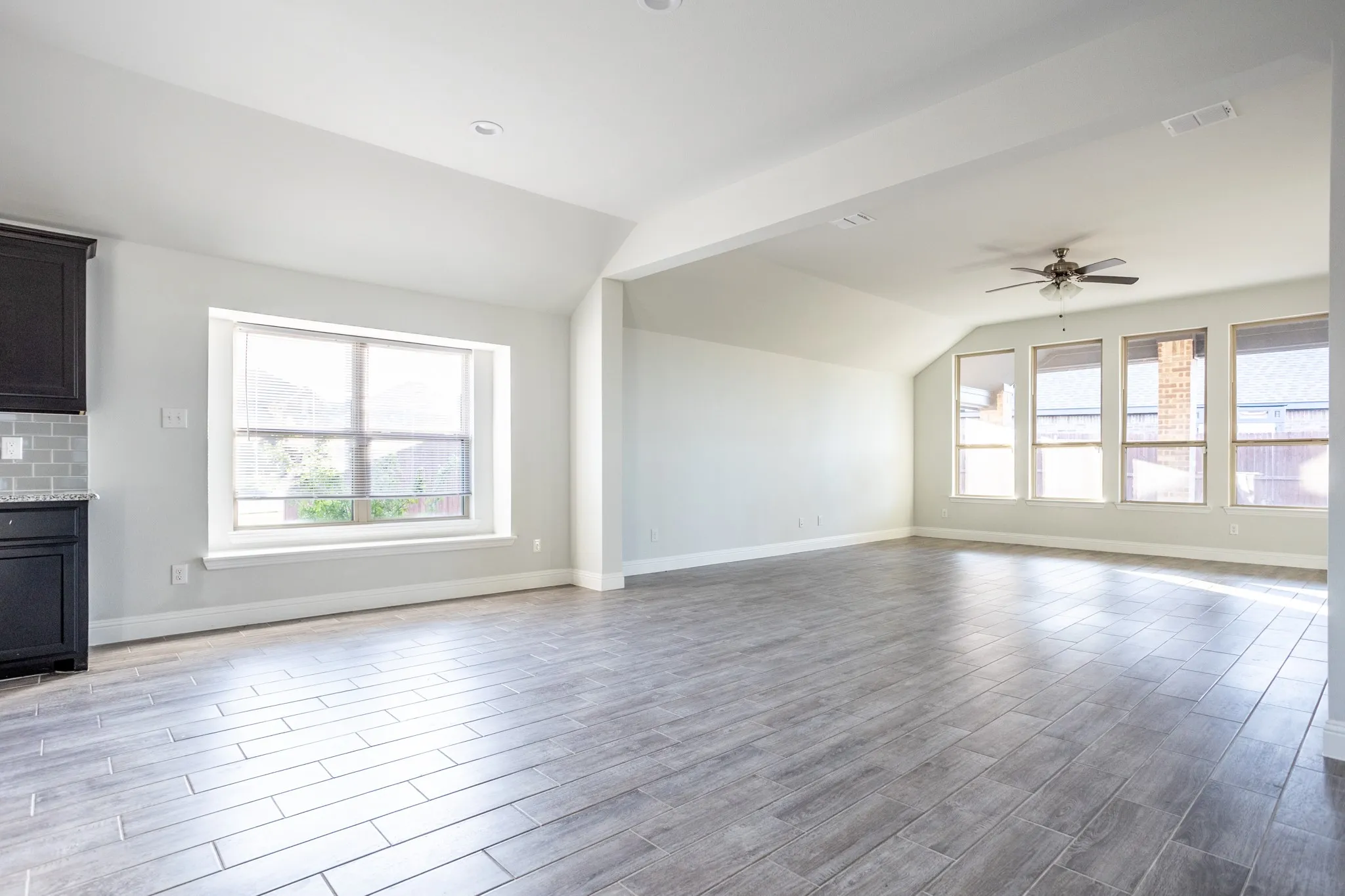 Spacious room featuring wood-finish tile flooring, a large window, a ceiling fan, and recessed lighting