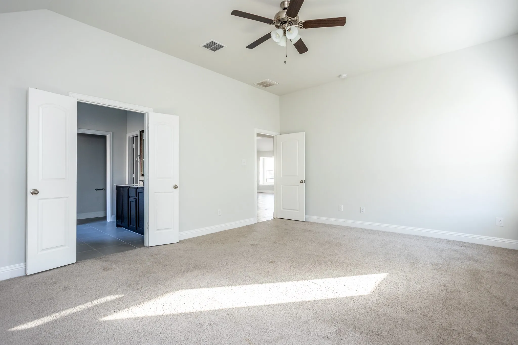 Vaulted ceiling, ceiling fan, neutral wall colors, light-toned carpeting, and a built-in vanity with a dark cabinet base