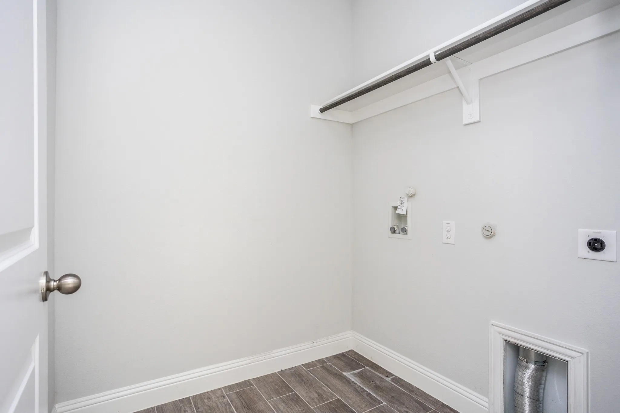 Dedicated utility space featuring a built-in hanging rod, wood-finish flooring, and essential appliance connections